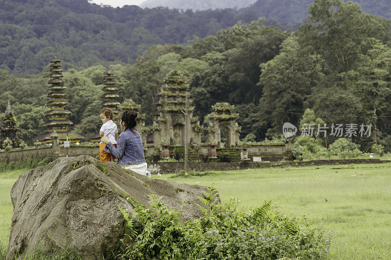 亚洲，印度尼西亚，巴厘岛，亚洲家庭坐在岩石上享受旅行，在坦布林安水庙前，一边观光。