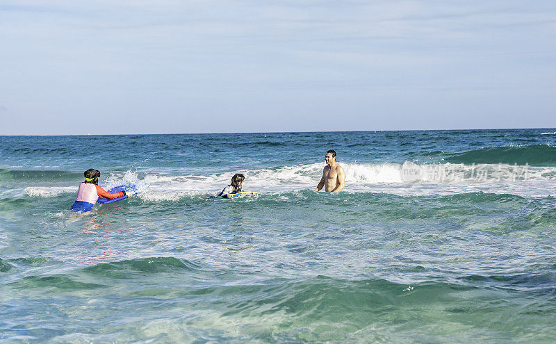 在一次热带度假中，爸爸和孩子们一起玩耍，教他们如何在海里冲浪