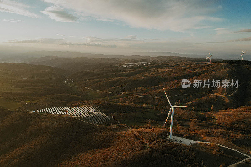 日落时的太阳能电池板和风力涡轮机。可再生能源