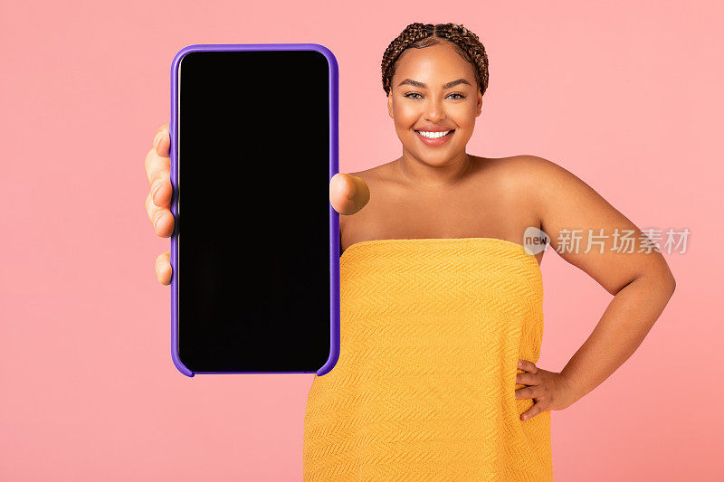 超重黑人女士展示智能手机巨大的空白屏幕，粉红色背景
