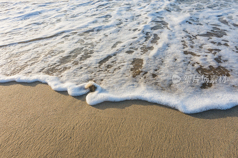 波浪与白色泡沫在沙滩上细沙在日出期间在埃及宏观
