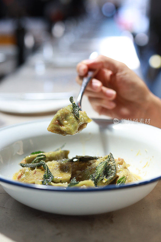 在一家餐馆里，一名亚洲妇女正在享用一碗菠菜agnolotti，里面有摩泰台拉干酪和乳清干酪，配上柠檬皮黄油酱。