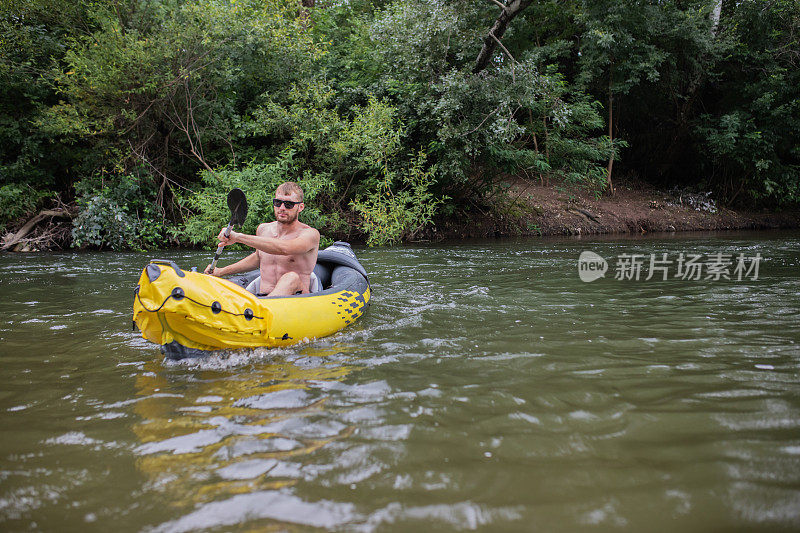 年轻的爱冒险的大胡子男子正用桨划着他的黄色充气独木舟在河上划船。