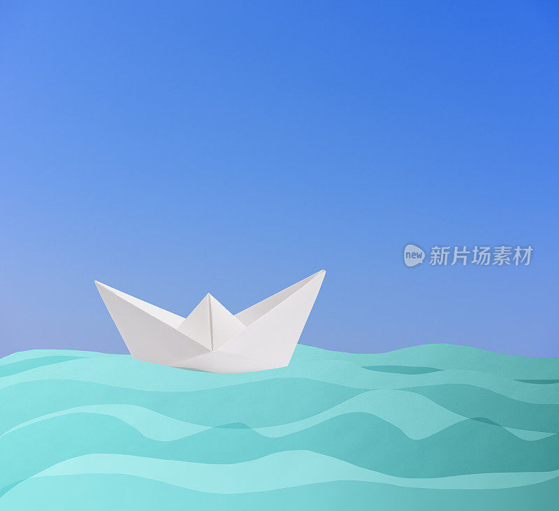 空白的折纸船航行在蓝色的纸浪对着晴朗的天空