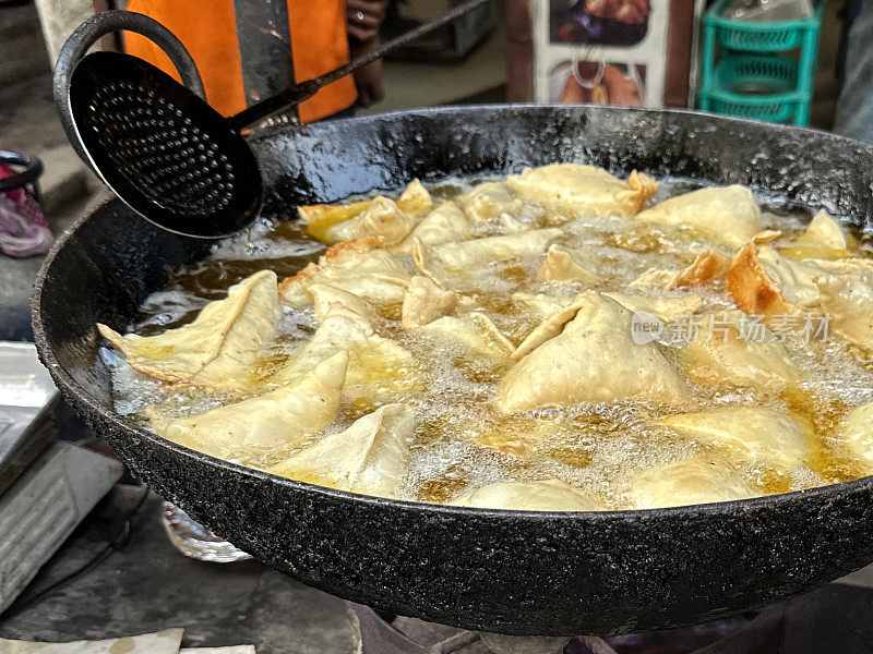 在karahi(印度炒锅)中油炸的一批samosas的特写图像，冒泡的热油，开槽的勺子，印度街头小吃摊，不健康的饮食，重点放在前景