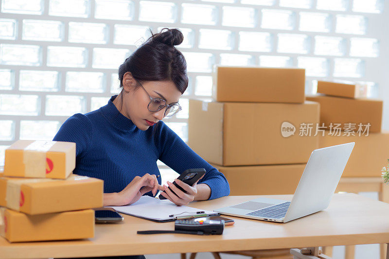 年轻的亚洲女性在网上为卖家提供送货服务，而女性在家里看智能手机，在文件上写客户的订单，在线送货，自由职业者做小生意。