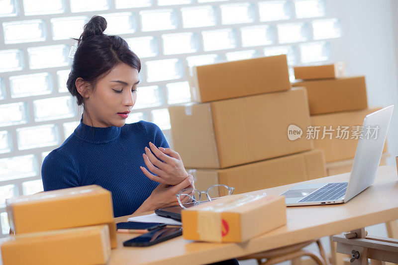 年轻的亚洲女性在网上销售送货服务，而女性办公室综合症的双手疼痛，因为在家里过度工作，网上航运，自由职业者做小企业或中小企业和零售。