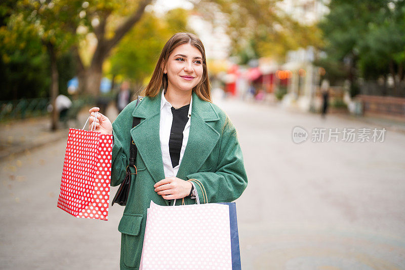 年轻的黑发女人在街上拎着购物袋。购物的概念