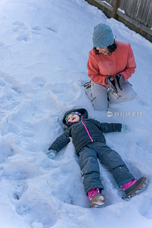 快乐的蹒跚学步的女孩和家人在雪地里玩耍时制作了一个雪天使
