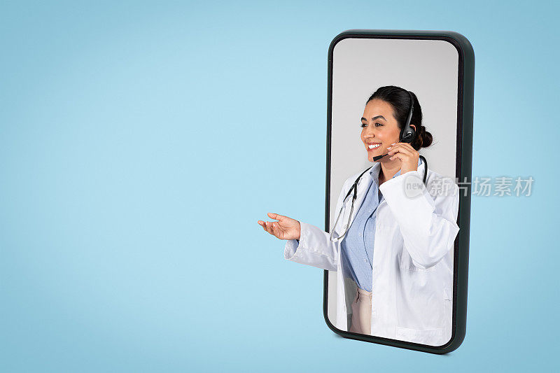 快乐的拉丁女医生戴着耳机在大屏手机上进行在线预约，蓝色背景，拷贝空间