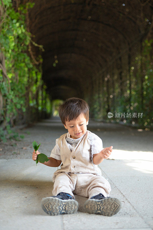 一个多种族的幼童心满意足地坐在公园的小路上