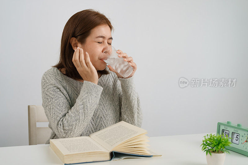 年轻的亚洲女子喝加冰的水，摸自己的脸颊，忍受牙痛，对寒冷有情绪反应。