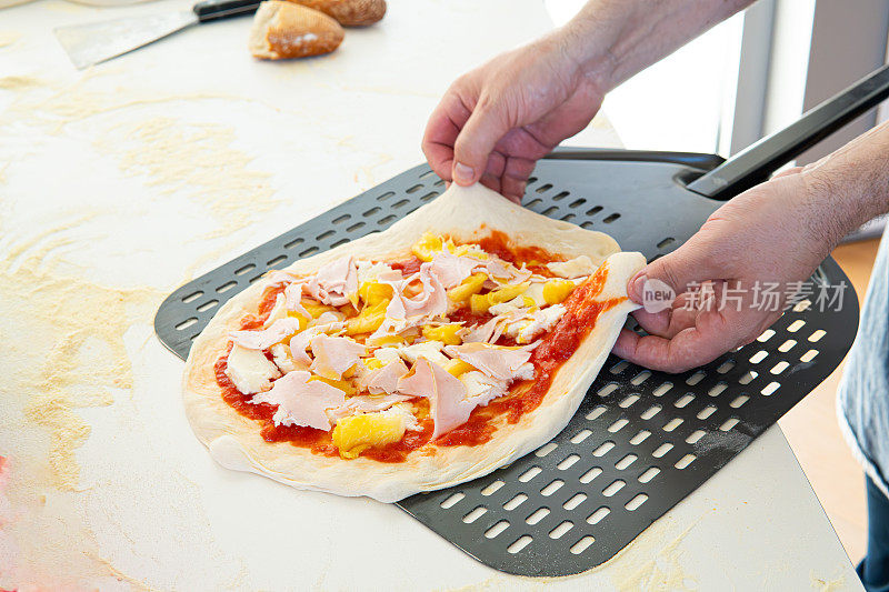 两只手将未煮熟的自制披萨放在特制的烤披萨皮上
