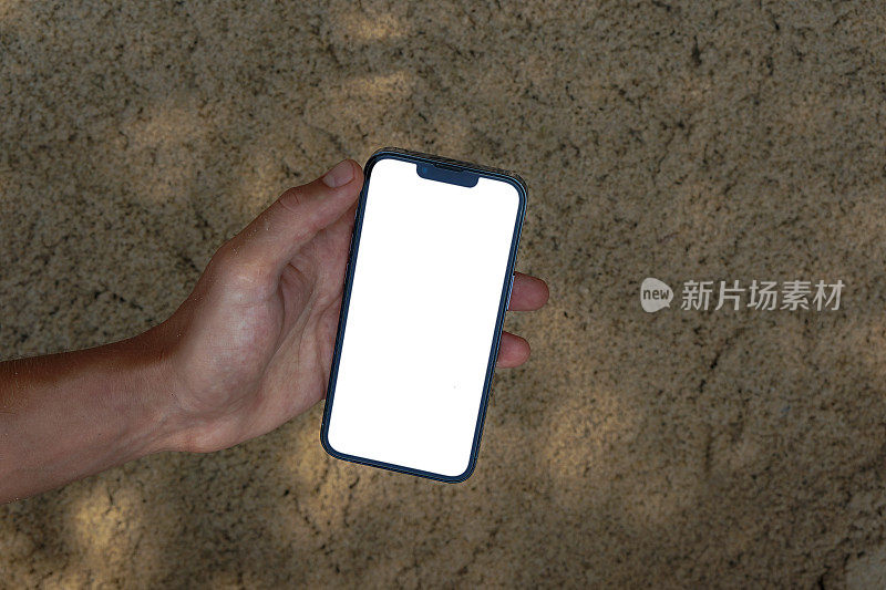 夏天的沙滩上，手拿着手机的白色空白屏幕