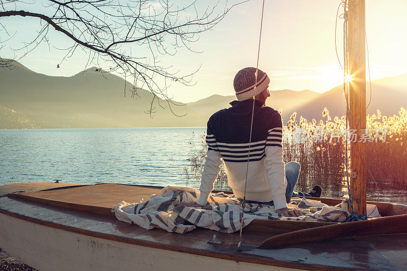 一个年轻人坐在湖边的帆船上看日落