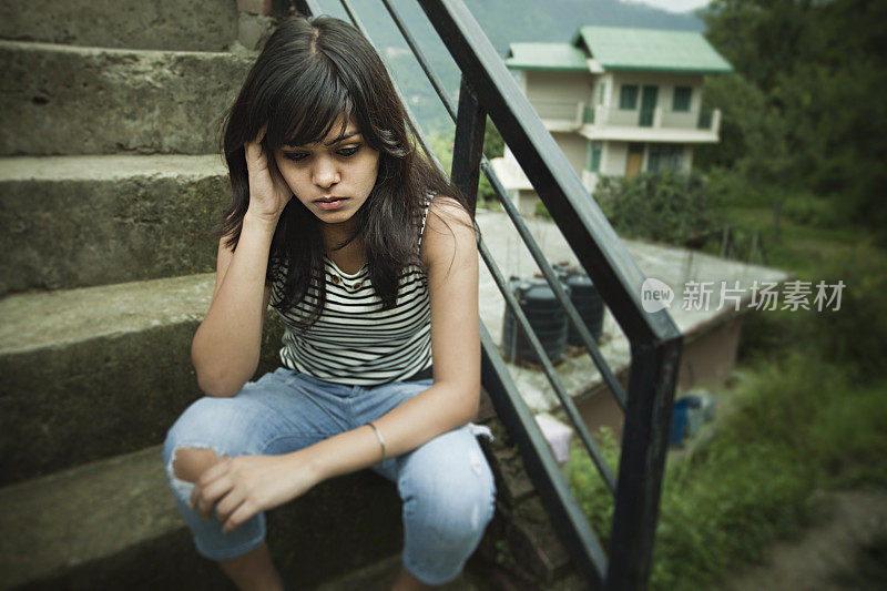 悲伤的亚洲女孩坐在丘陵地区的台阶上。