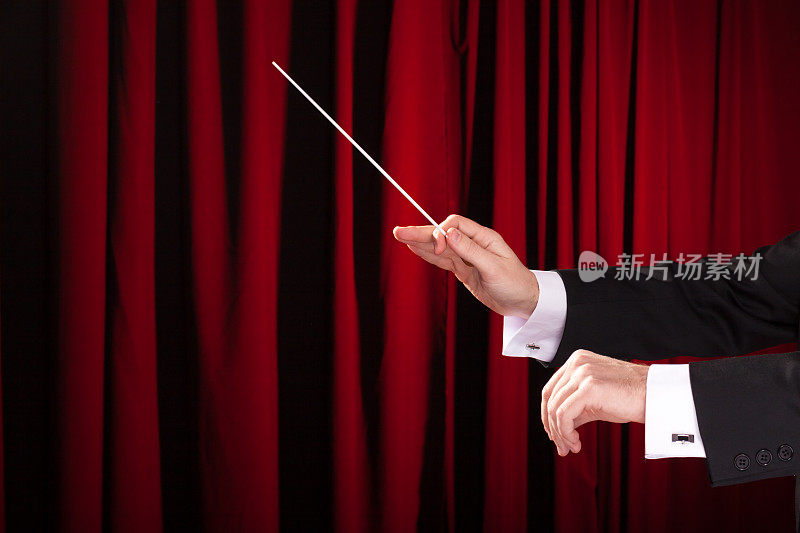 一个男性音乐指挥的手拿着一根魔杖和红色的窗帘