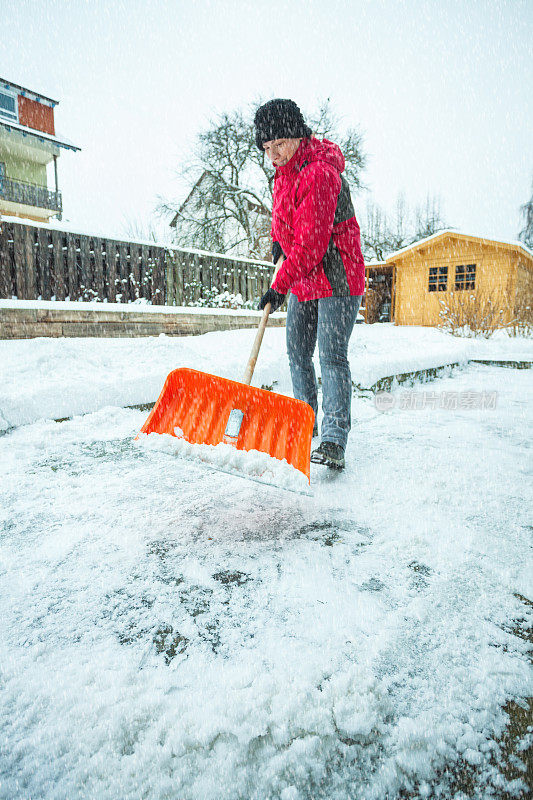 一位中年妇女正在清理屋前的积雪