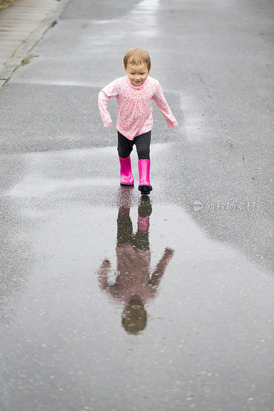 穿着雨靴的小女孩正要穿过水坑