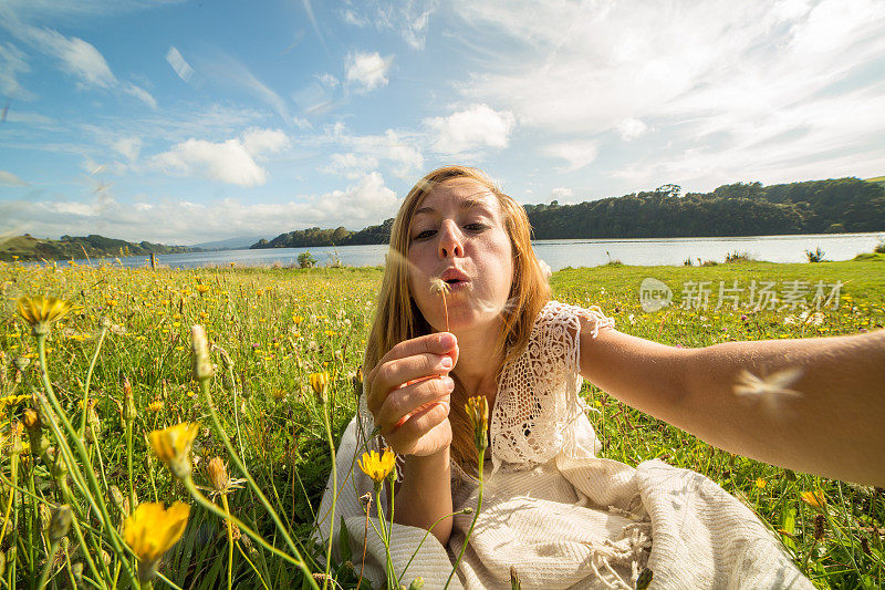 一名女子在草地上吹花时自拍