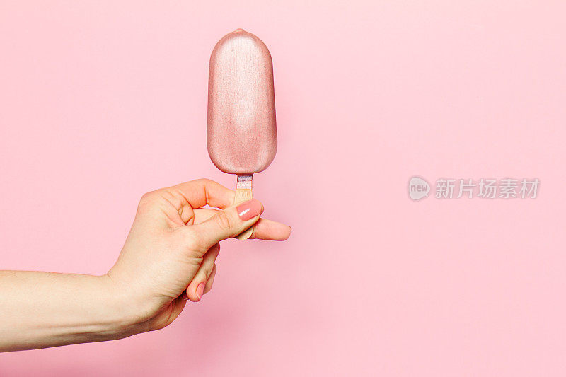 一个年轻女子的手拿着冰淇淋在粉红色的背景。
