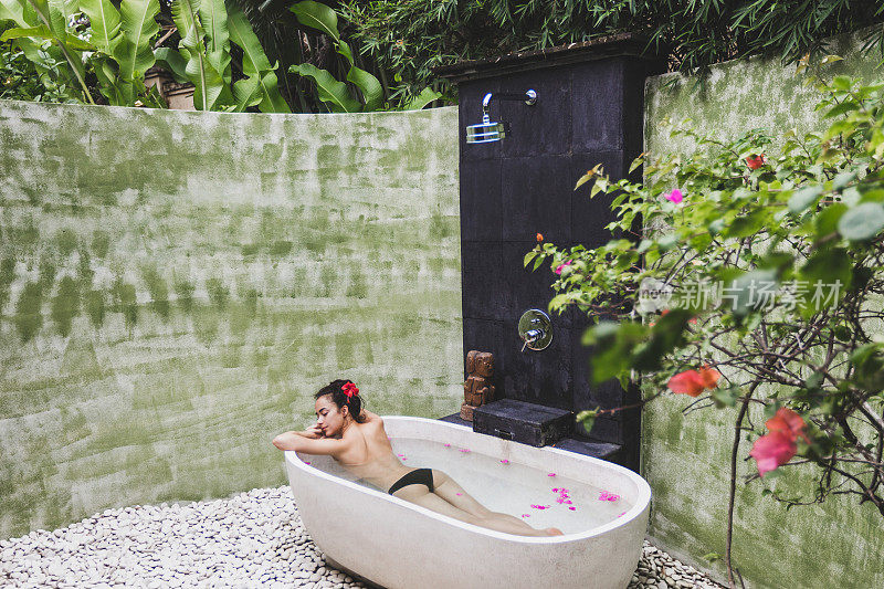 女人放松在圆形户外沐浴热带鲜花，有机皮肤护理，豪华水疗酒店，生活方式照片