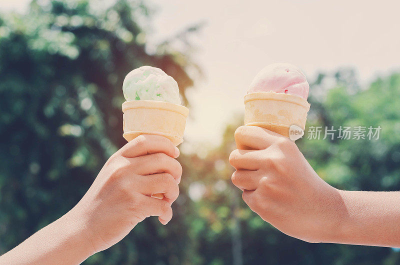 孩子们的手拿着冰淇淋蛋筒在夏季光自然背景