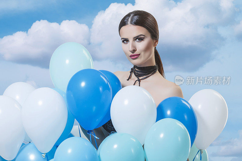 年轻的女人拿着一堆氦蓝色的气球对着天空夏天的时尚