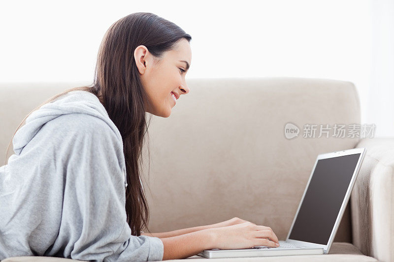 一个面带微笑的女人躺在她的前面使用她的笔记本电脑