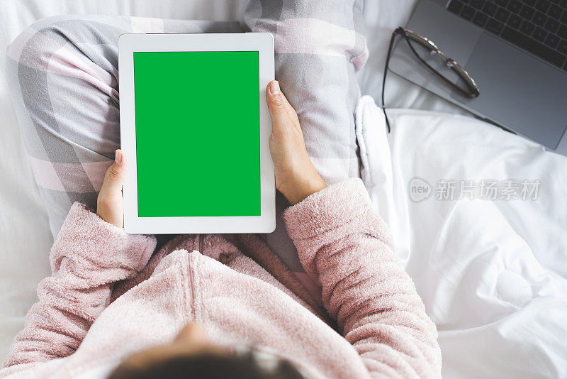 女人坐在床上，使用绿色屏幕的数字平板电脑