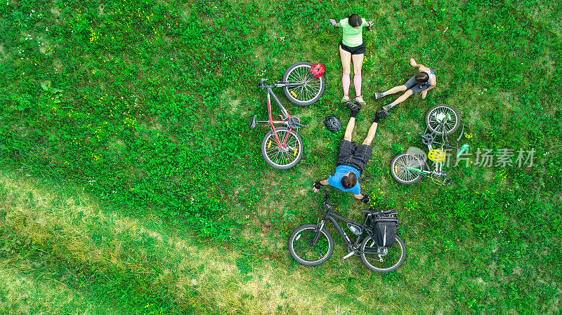 家庭在户外骑自行车鸟瞰图从上面，快乐活跃的父母和孩子有乐趣和放松在草地上，家庭运动和健身周末