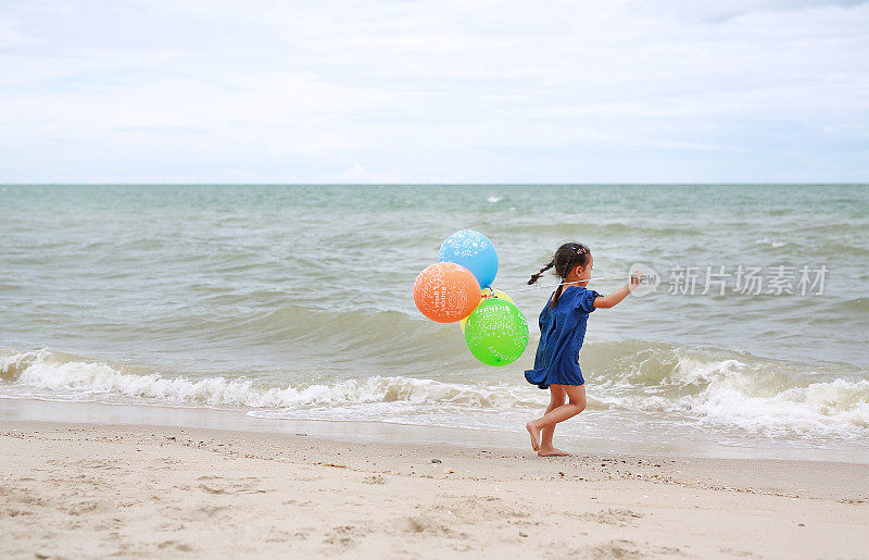 小女孩拿着彩色气球在沙滩上奔跑。