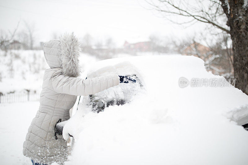 一位妇女正在清理一辆被雪覆盖的汽车。在大雪堆周围