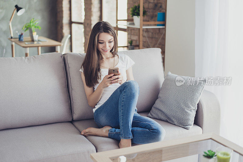 一个年轻漂亮的女人坐在家里的沙发上给她的男朋友发短信