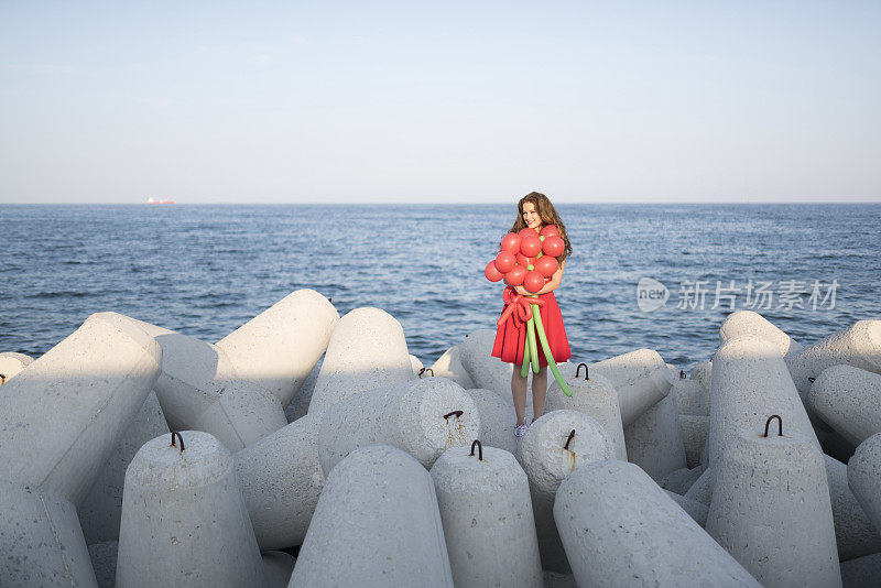 快乐的女士穿着红色的裙子和一个大气球花束在海边