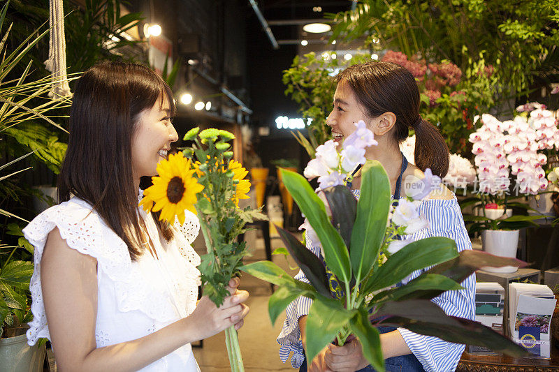 在花店里帮助一位挑选向日葵和树叶的妇女的店员。