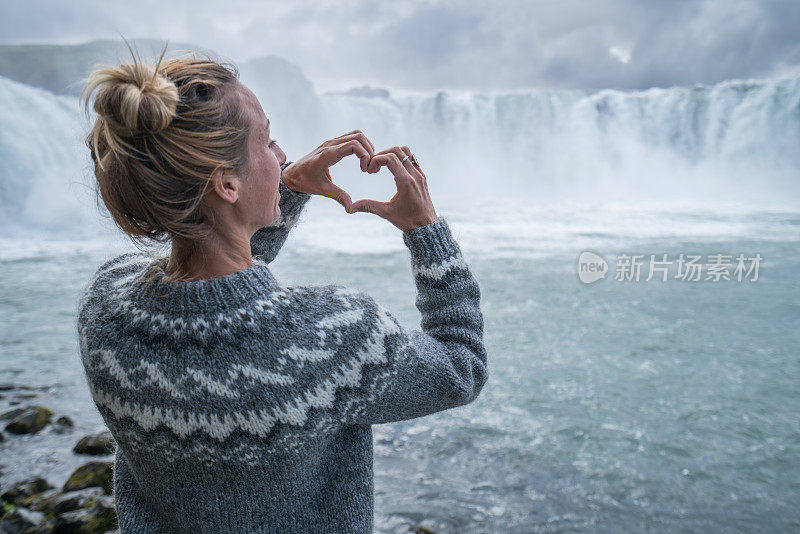 一名冰岛年轻女子在壮观的瀑布上制作心形手指架