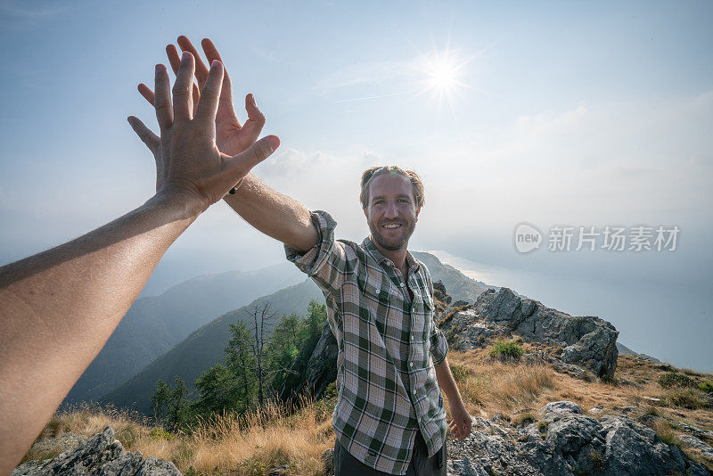 两个徒步旅行者在山顶击掌庆祝的个人视角