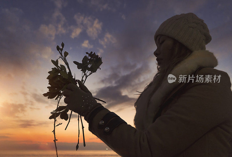 日落时分，女人在海滩上向大海抛下鲜花