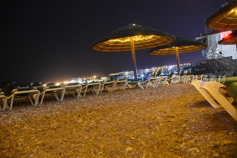晚上在海边，戴着遮阳伞，坐着沙滩椅