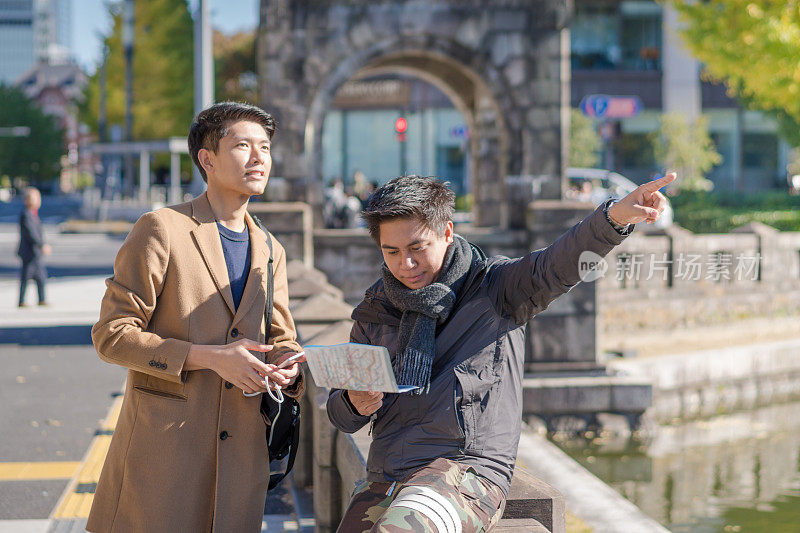 年轻的亚洲男子和日本朋友寻找旅游地点使用手机和花时间在亚洲旅行