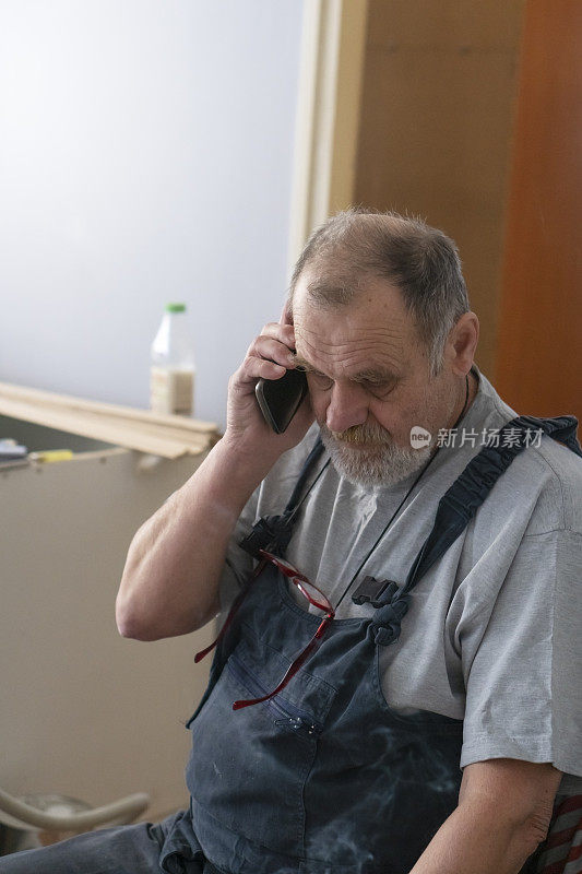 一位老人正在翻新他的公寓，并在使用智能手机