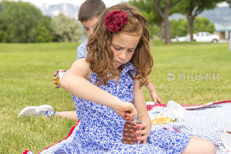 可爱的红发小女孩在公园野餐时打开汽水罐