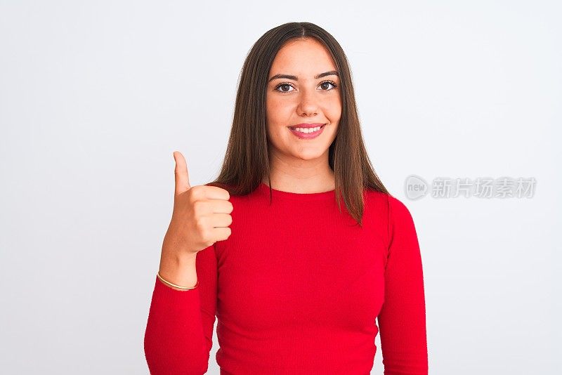 年轻美丽的女孩穿着红色休闲t恤站在孤立的白色背景做快乐的拇指向上的手势与手。赞许的表情看着镜头，表示成功。