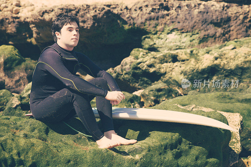 一个带着冲浪板坐在长满青苔的岩石上的人