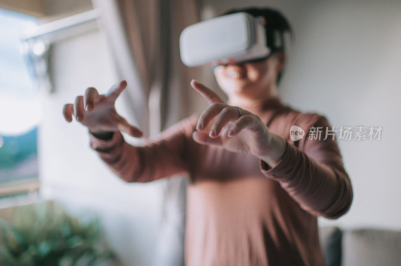 一个亚裔中国中年女性在客厅里使用VR谷歌玩VR虚拟现实在线游戏