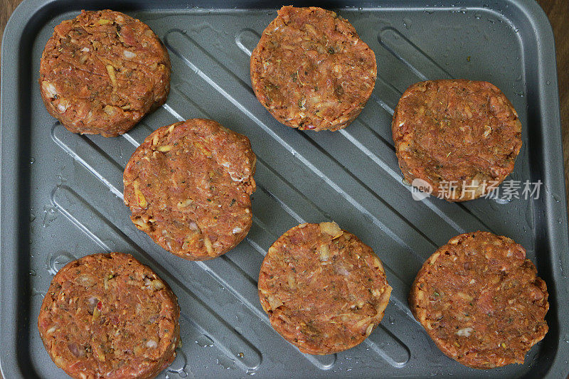 图为一排排自制的生牛肉饼，在厨房台面上的烤盘准备在烤箱中烹饪