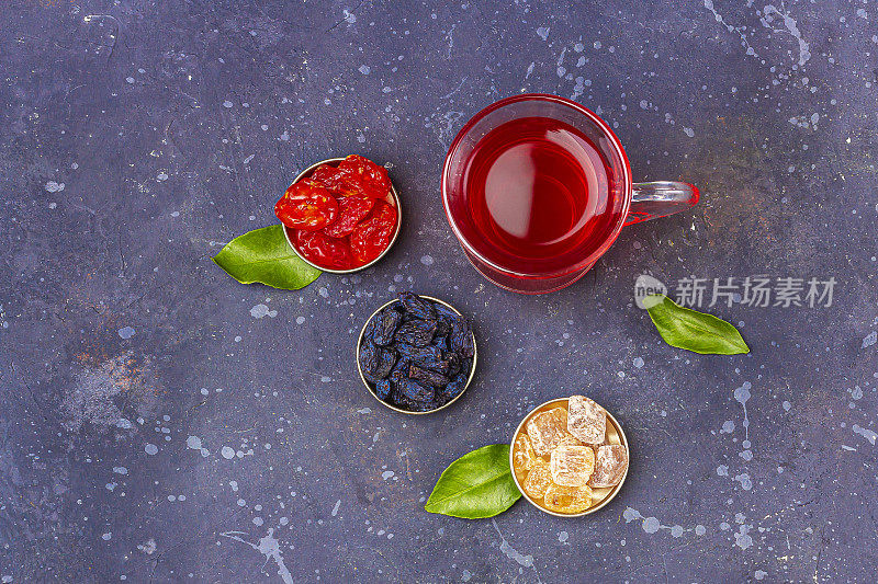 土耳其茶杯(armudu)中红茶(roibos，木槿，karkade)与山茱萸，葡萄干，糖在深色的背景上。草药，维生素，治疗感冒和流感的排毒茶。文本复制空间