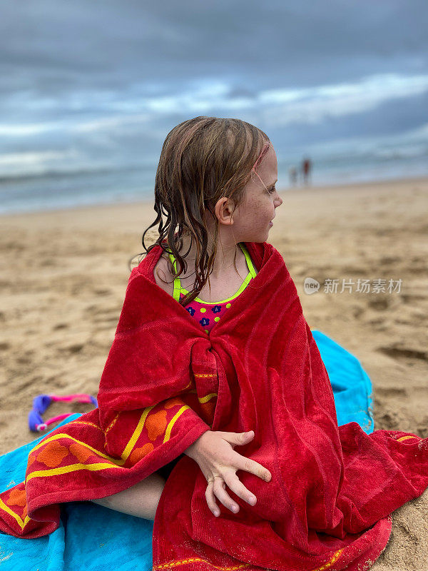 年轻女孩裹着一条红毛巾坐在海滩上
