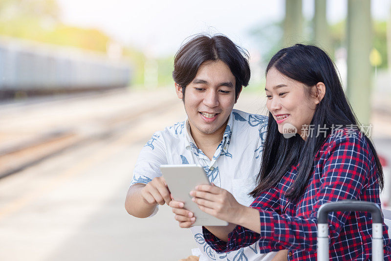 年轻的亚洲夫妇背包客使用平板电脑寻找目的地旅行在火车站